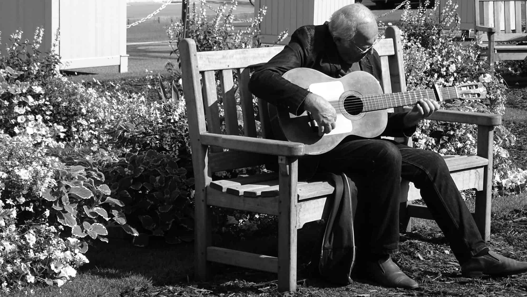 a senior man sitting on a bench playing the acoustic guitar - are you too old to learn guitar?